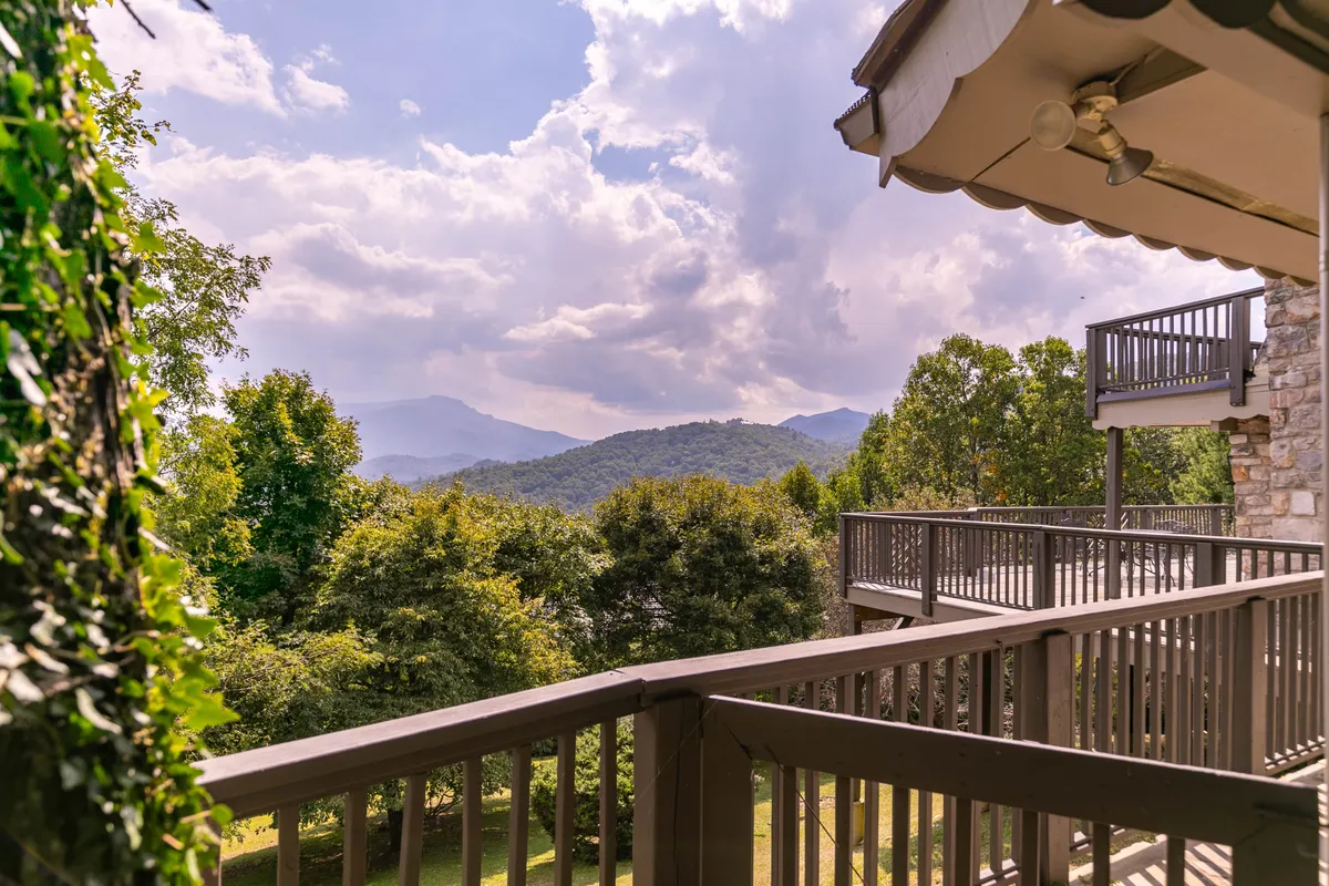 A breathtaking mountain range view from a deck or balcony, framed by a railing and lush greenery. The foreground invites you to imagine enjoying a morning coffee or quiet contemplation while soaking in the vista.