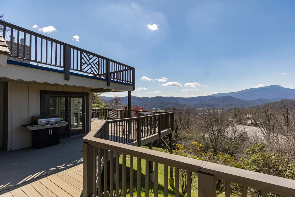 An expansive outdoor deck featuring a sturdy railing, stainless steel grill, and alfresco dining setup, all overlooking a dramatic mountain panorama. The space is perfect for sunset meals and outdoor gatherings.