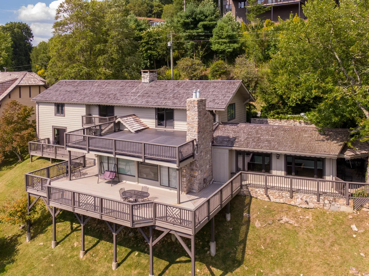 An exterior view of the house with a large deck, a striking stone chimney, and a backdrop of tall, leafy trees. The atmosphere is tranquil and welcoming, emphasizing the home's connection to nature and providing a sense of place in the high country.