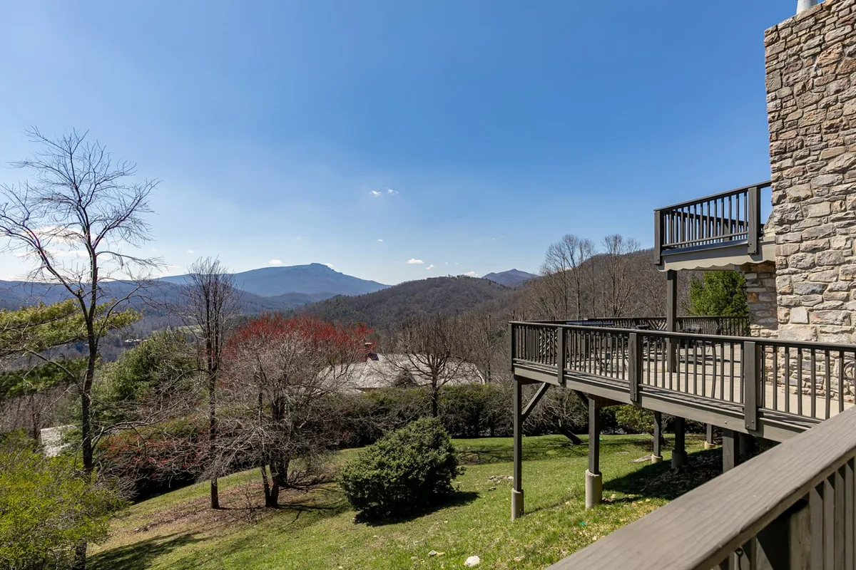 A serene exterior scene featuring a deck overlooking layered mountain ranges, surrounded by greenery. The inviting deck space is outfitted for relaxation, ideal for wildlife watching, sunset views, or intimate outdoor dining.