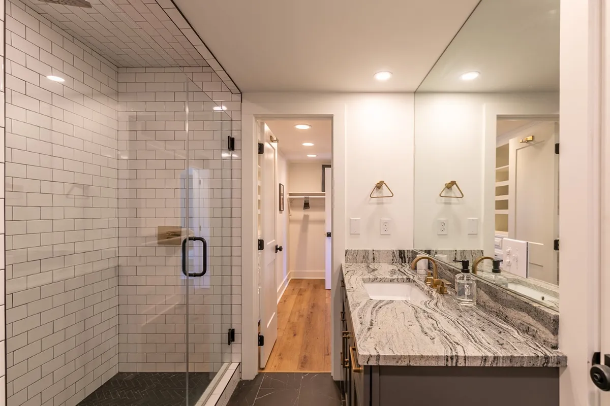 A sophisticated modern bathroom with a glass shower enclosure, marble countertop, and elegant gold fixtures, exuding a clean, calm, and luxurious atmosphere.