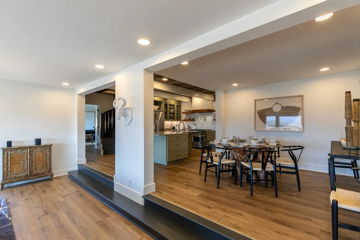 A dining area set for a meal, adjacent to the kitchen with visible modern appliances and decorative wall art. The table is ready for a gathering, suggesting a space where guests can enjoy meals together.