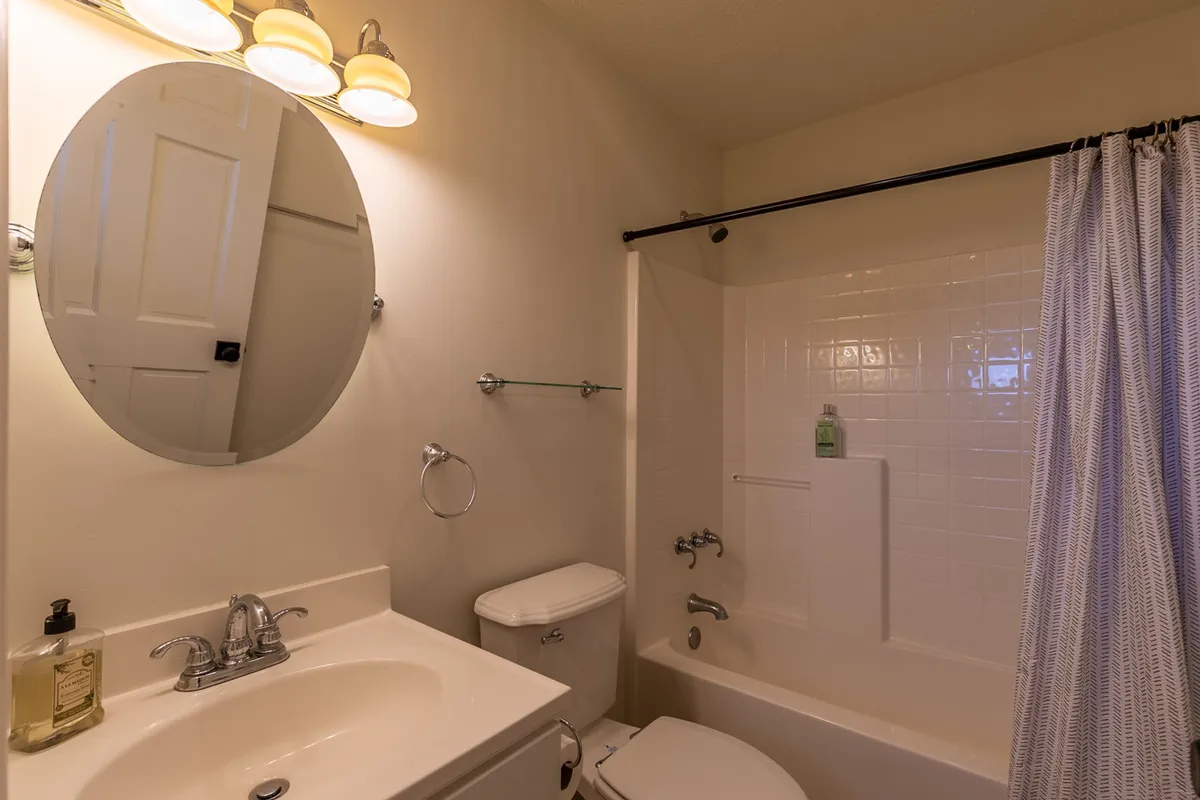 This image features a modern, practical bathroom with a large mirror, sink, and a spacious shower area. The neutral color palette and clean lines emphasize calm and functionality, making it a comfortable space for self-care routines.