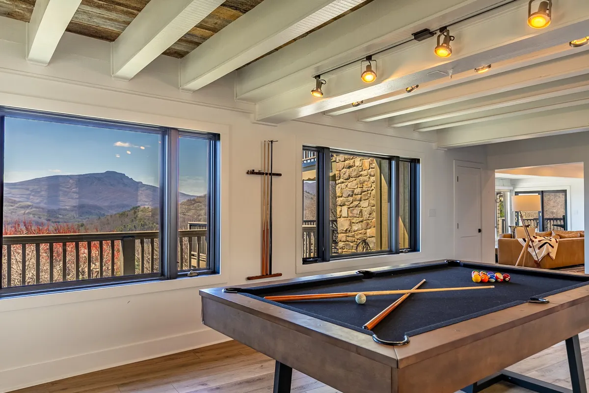 A stylish game room with a pool table situated in front of large windows that offer panoramic mountain views. The room fosters a relaxed, recreational atmosphere, ideal for socializing and enjoying the scenery while playing games.
