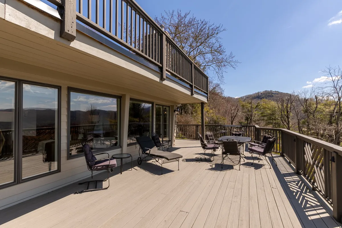 This image shows a spacious deck outfitted with comfortable chairs and a table, all oriented toward a sweeping mountain vista. Large windows connect the deck and the house, blurring the line between indoors and outdoors. The tranquil setting is ideal for relaxing, socializing, or simply soaking in the natural beauty.
