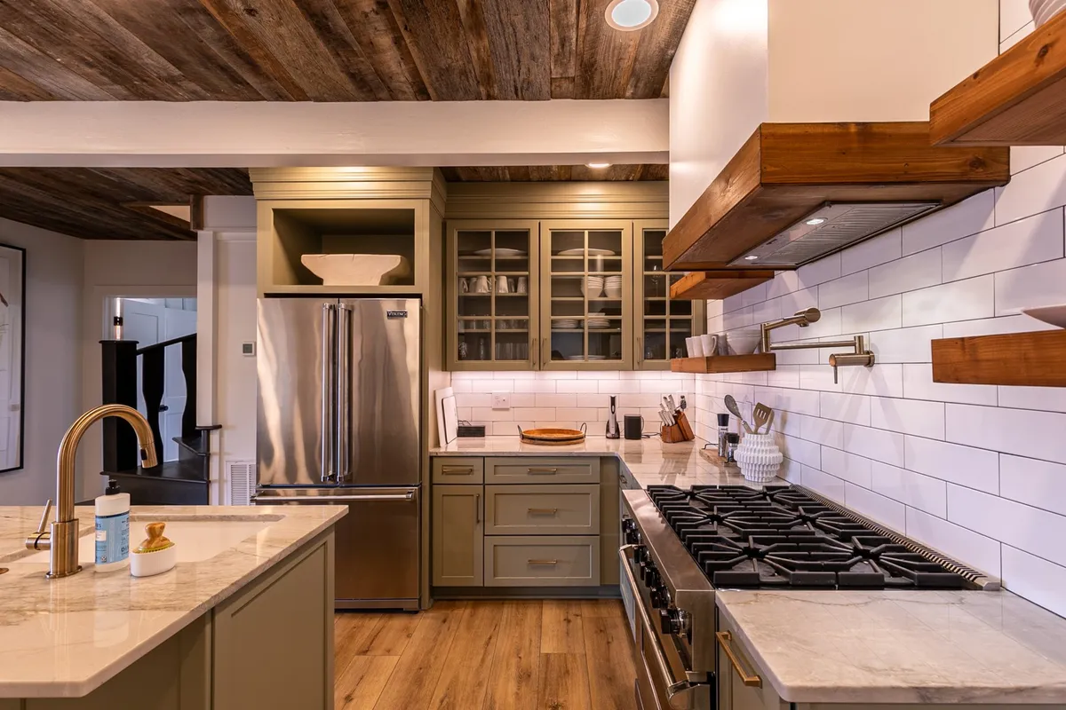 A welcoming kitchen scene with prominent stainless steel appliances, an expansive kitchen island, open shelving, and a warm wooden ceiling. The modern yet homey atmosphere is perfect for cooking and entertaining.