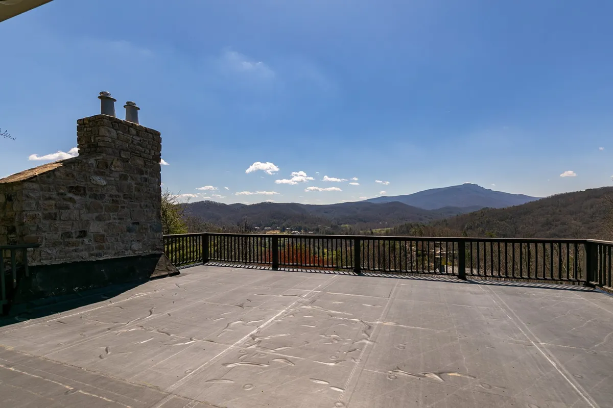 A breathtaking view of the mountains is framed by a stone chimney and balcony railing, with soft light bathing the landscape. The inviting outdoor space is perfect for morning coffee, evening gatherings, or stargazing, echoing the private, elevated experience of the home.